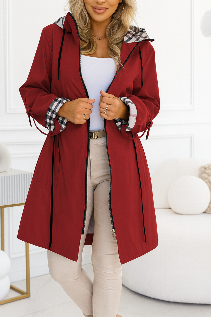 Woman wearing a red coat with plaid accents in a white room.